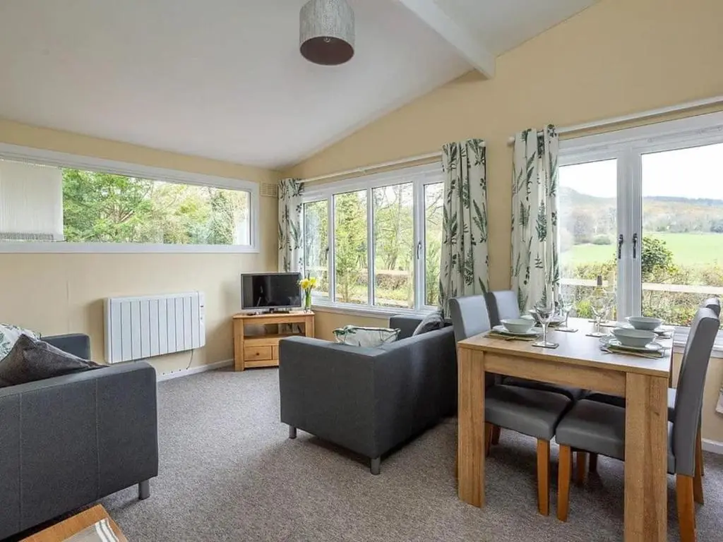 a living room with a table and chairs and windows at Bridgend Chalet on Reelig Estate in Kirkhill