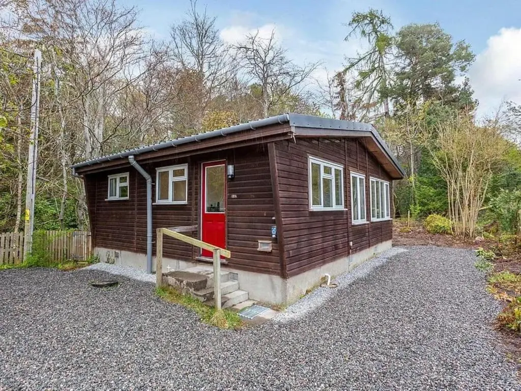 a small cabin with a red door in the woods at Bridgend Chalet on Reelig Estate in Kirkhill
