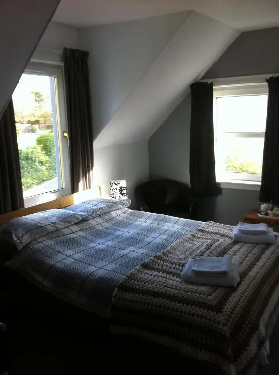 a bedroom with a bed with a blue blanket and two windows at The Whitehouse in Dingwall