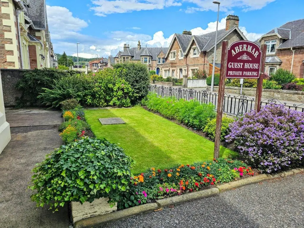 a sign for a guest house with flowers in a yard at mySTAYINN Abermar 12 Bedroom House in Inverness