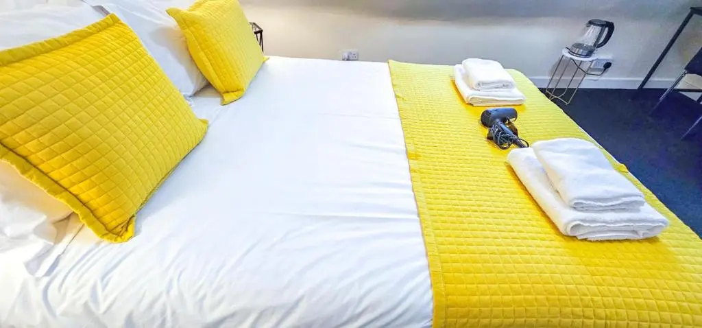 a white bed with yellow pillows and towels on it at mySTAYINN Telford Guest House in Inverness