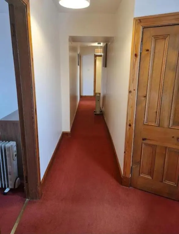 an empty hallway with a wooden door and red carpet at Ness City Apartment in Inverness