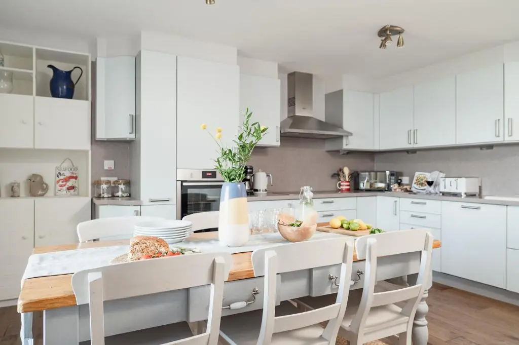 a kitchen with white cabinets and a table and chairs at Ina's Cottage - Seasgair Lodges in Portmahomack