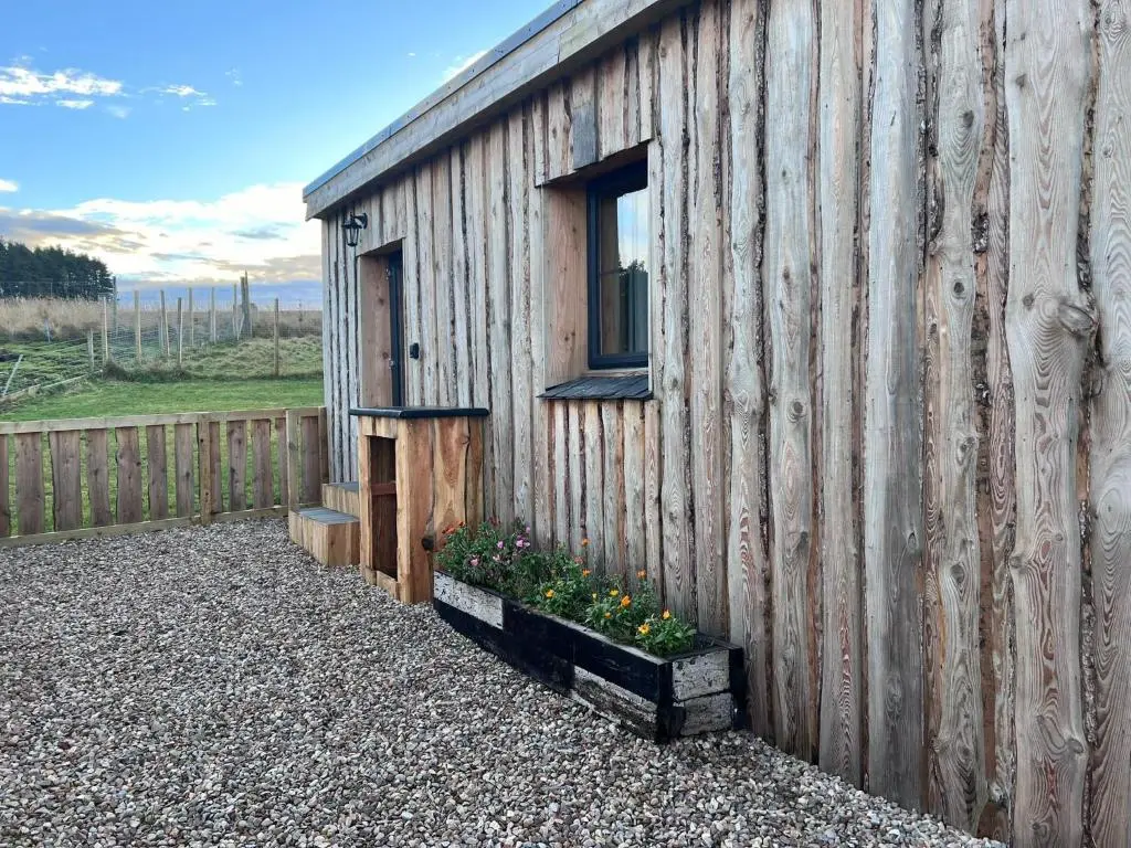 a small wooden building with a window and some flowers at Honeysuckle Straw Bale Cabin