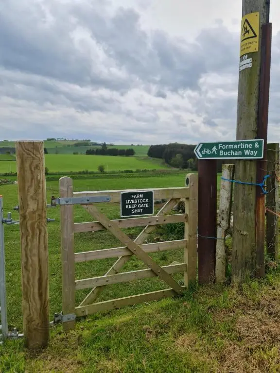 a wooden gate with a sign on it next to a field at Bruxie Holiday Cottages - River Cottage in Maud