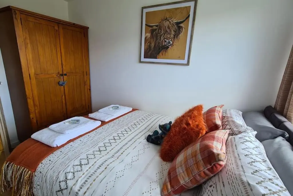 a bed with towels and a picture of a cow on the wall at Northlea-Scottish style cottage in Inverness