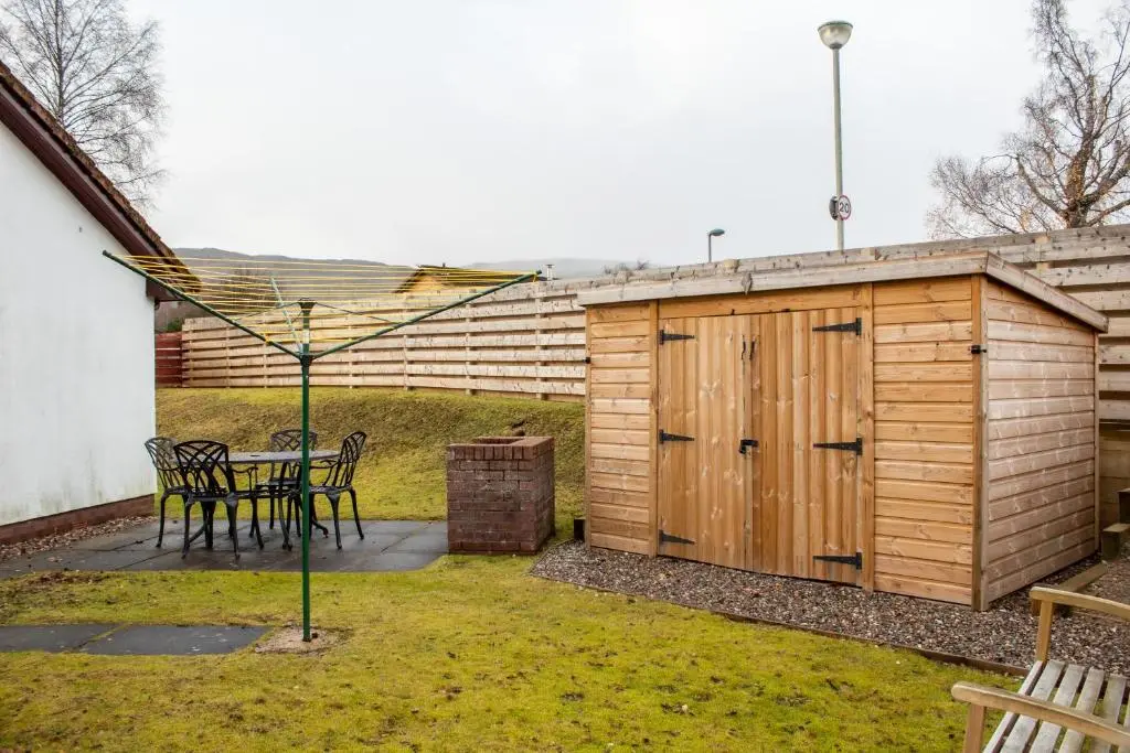 a patio with a table and a wooden shed at Pine Marten Cottage - Aviemore in Aviemore