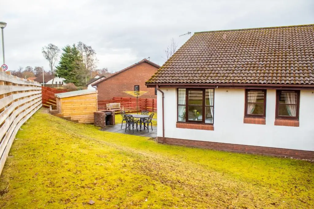 a white house with a table in a yard at Pine Marten Cottage - Aviemore in Aviemore