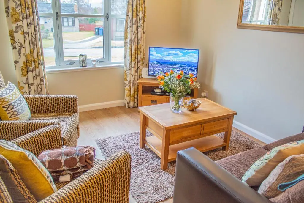 a living room with a tv and a table with flowers at Pine Marten Cottage - Aviemore in Aviemore