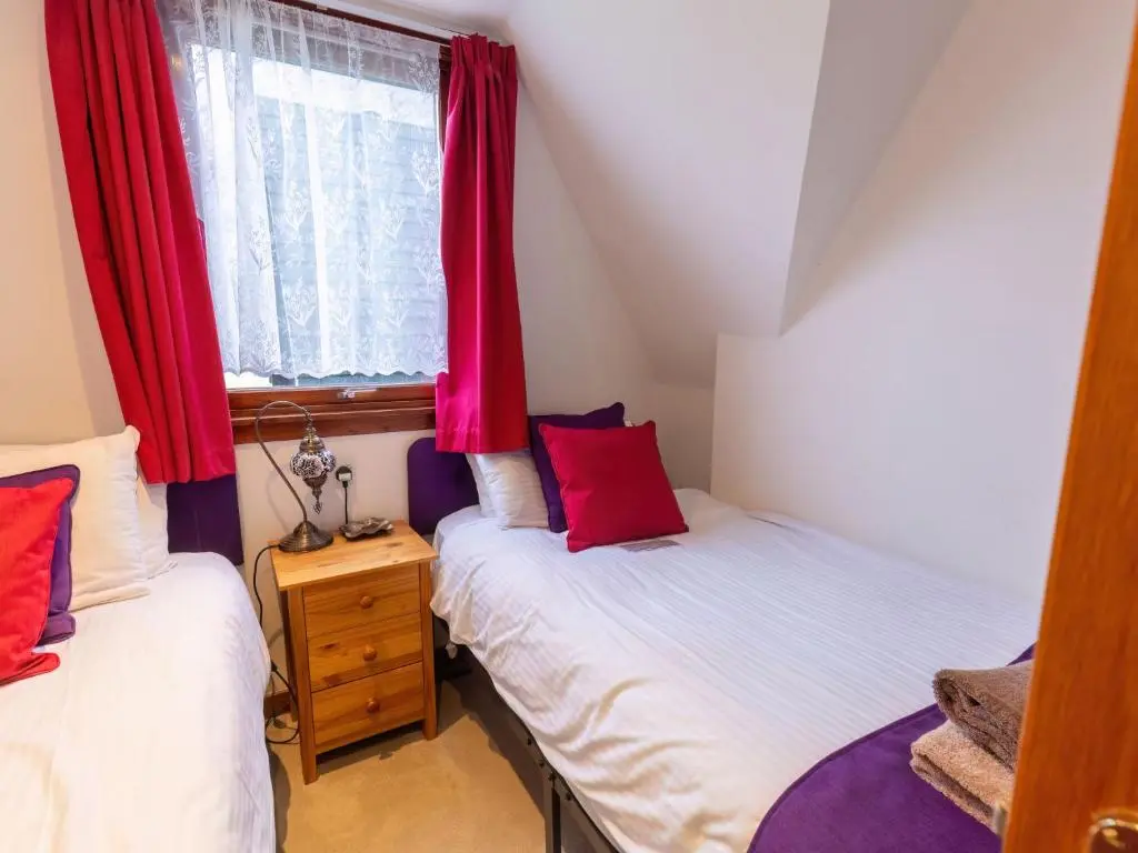 two twin beds in a room with red curtains at Chalet Lothlorien Lodge 4 by Interhome in Spean Bridge