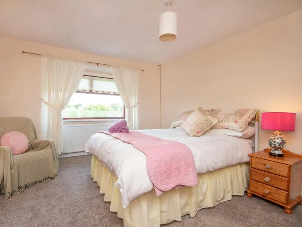 a bedroom with a bed and a chair and a window at Black Rock Cottage in Culbokie