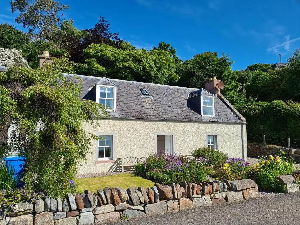 a white house with a stone wall and flowers at Braefoot in Fortrose