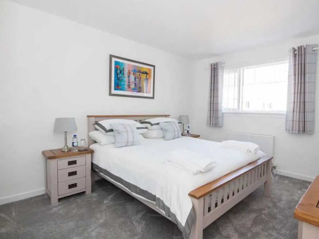 a white bedroom with a large bed and a window at Raasay in Dornoch