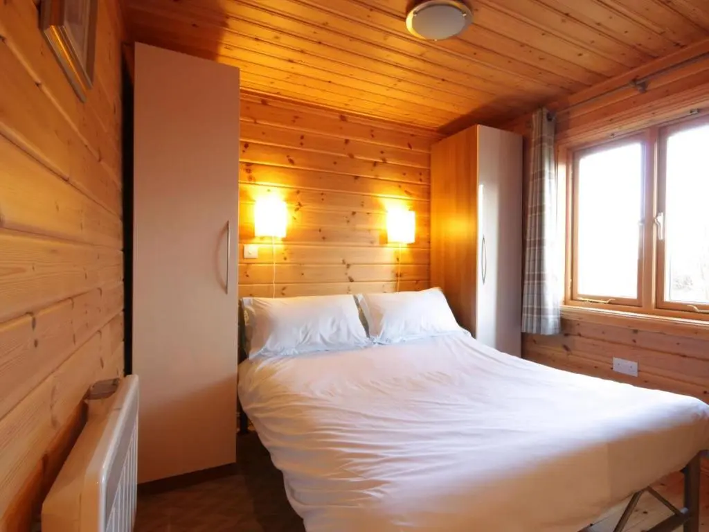 a bedroom with a white bed in a wooden room at Taigh Fiodha in Balintore