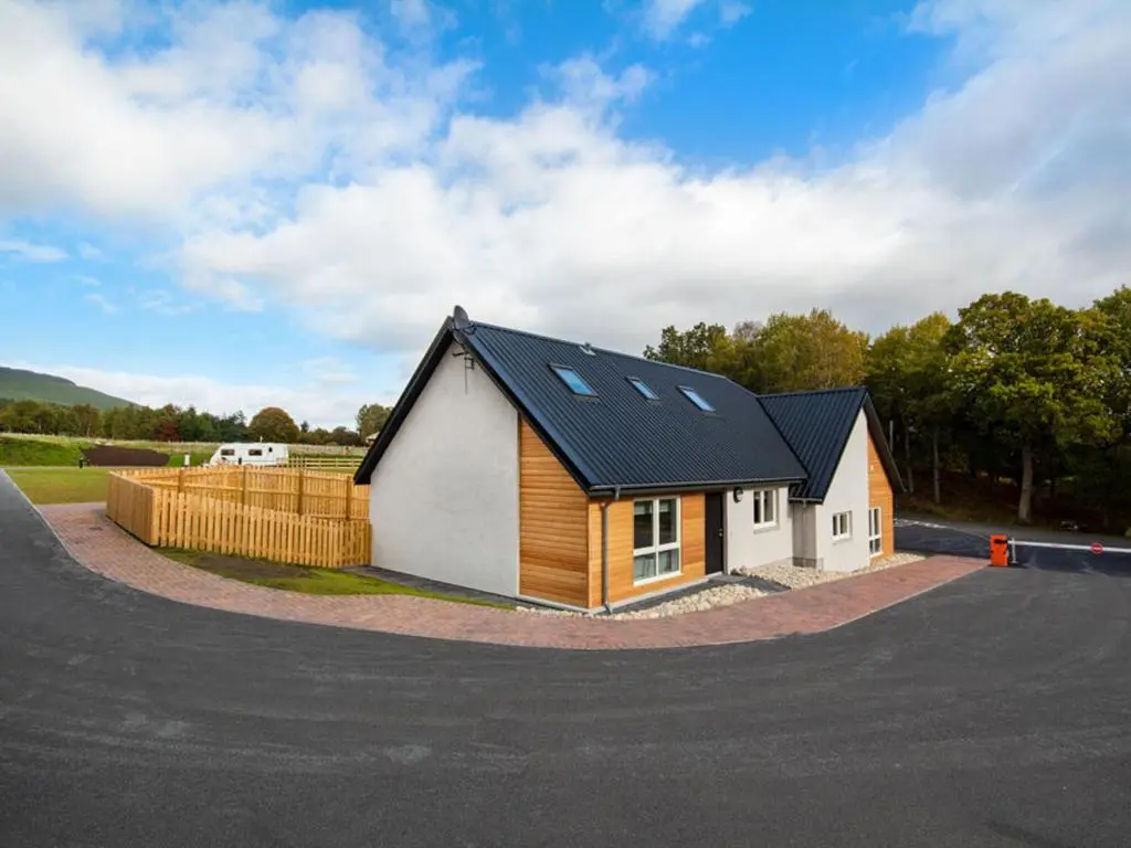 a small house with a black roof on a road at Oakwood in Aviemore