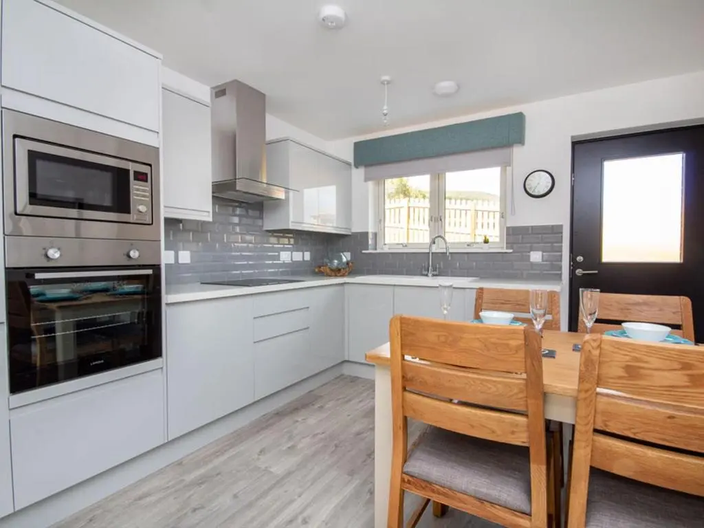 a kitchen with white cabinets and a table with chairs at Oakwood in Aviemore