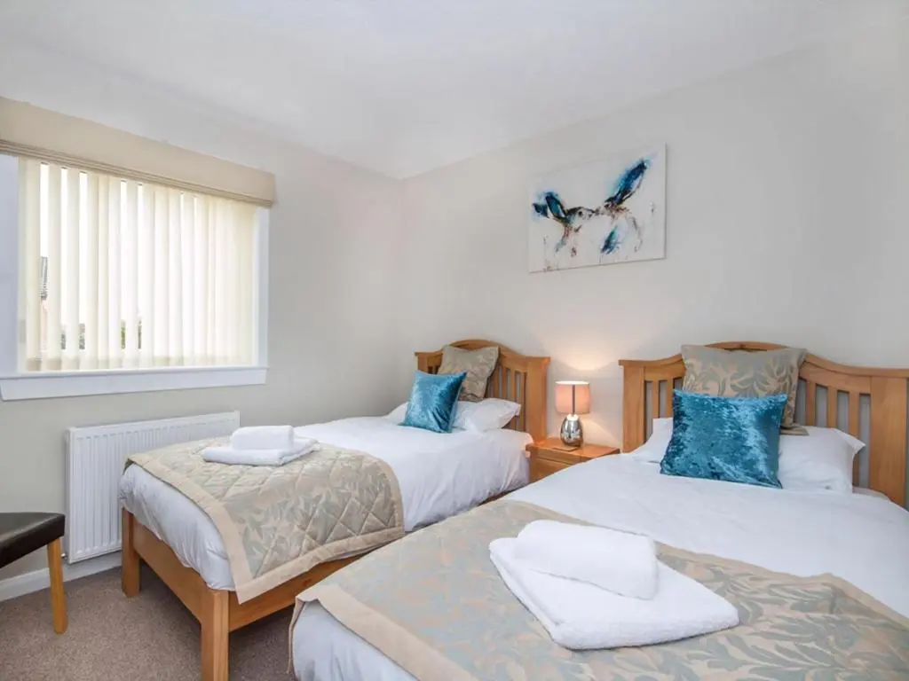 two beds in a bedroom with blue pillows at 58 Moray Park in Culloden