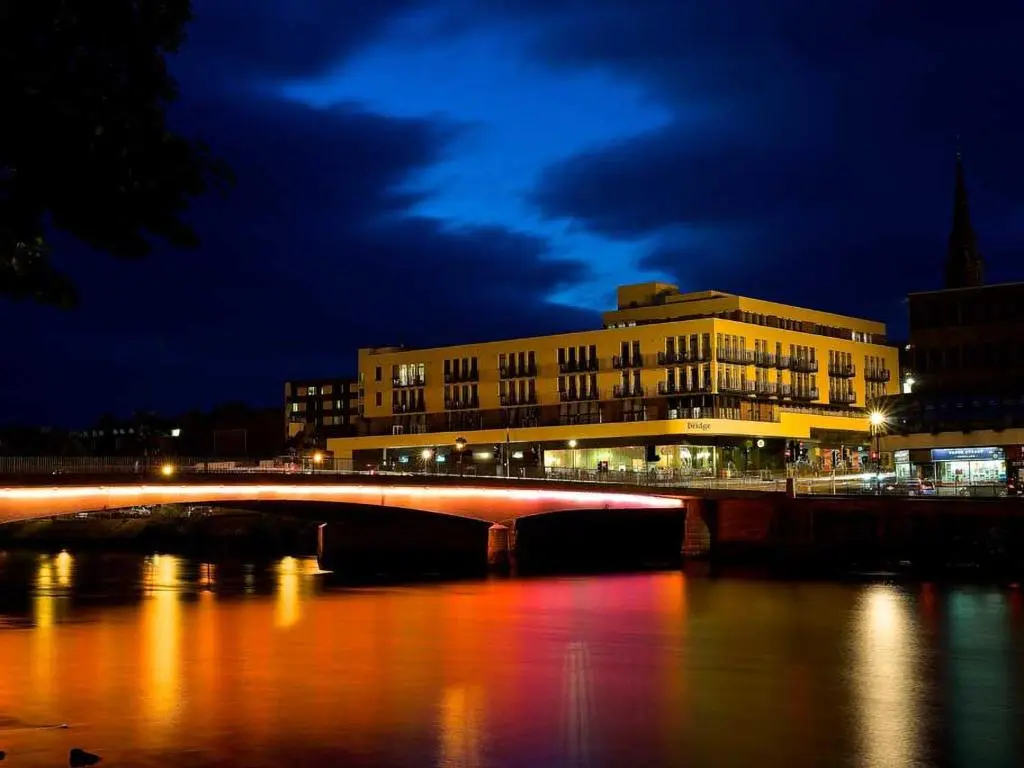 a bridge over a river in front of a building at 206 By The Bridge Apartment in Inverness