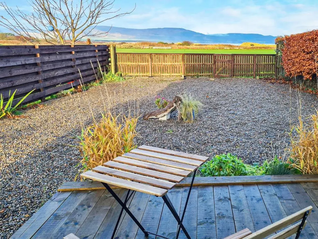 a wooden bench in a garden with a fence at Sunnyside Cottage in Embo