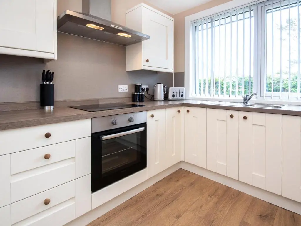 a white kitchen with white cabinets and a sink at Colbheinn Cottage in Brora