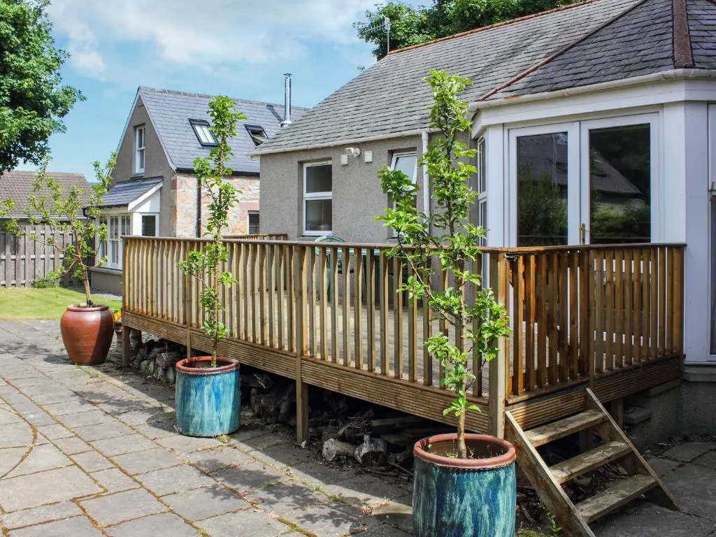 a house with three potted trees in barrels next to a fence at Pine Tree Cottage - Uk45925 in Ballater