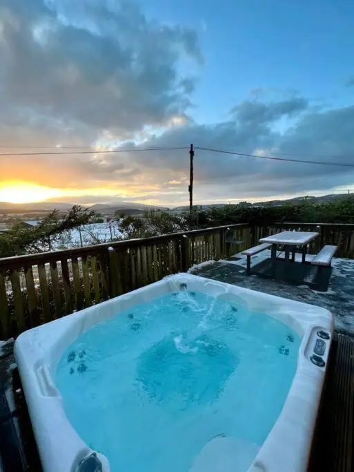 a hot tub on a deck with a sunset in the background at Luxury Lodge With Hot Tub In Royal Deeside in Strachan