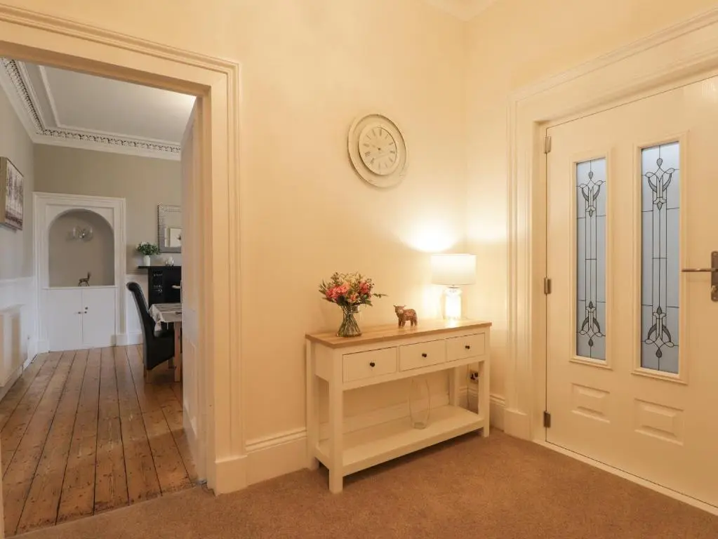 a hallway with a door and a vase of flowers on a table at Arden House in Kingussie