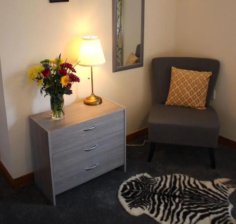 a room with a dresser with a vase of flowers and a chair at Taigh Munro in Aviemore