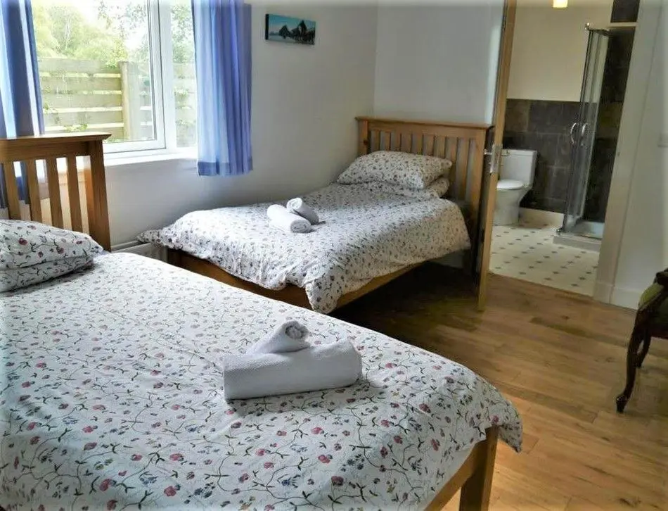 two twin beds in a room with a bathroom at Osprey Cottage in Aviemore