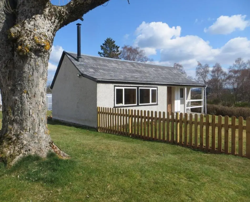 a white house with a fence and a tree at Sycamore Cottage in Boat of Garten