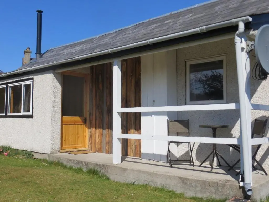 a small house with a wooden door and a porch at Sycamore Cottage in Boat of Garten
