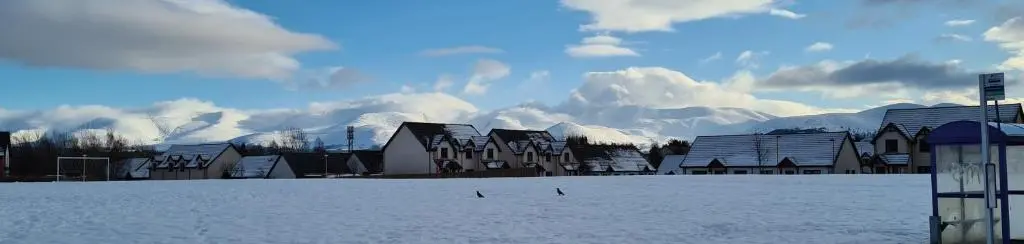a snowy field with buildings and mountains in the background at Mountain View No12 in Aviemore