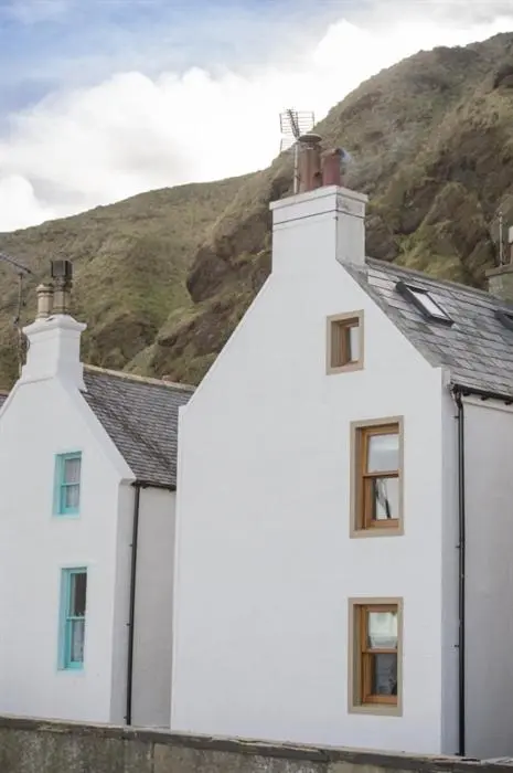 a white house with a mountain in the background at The Wee House in Pennan