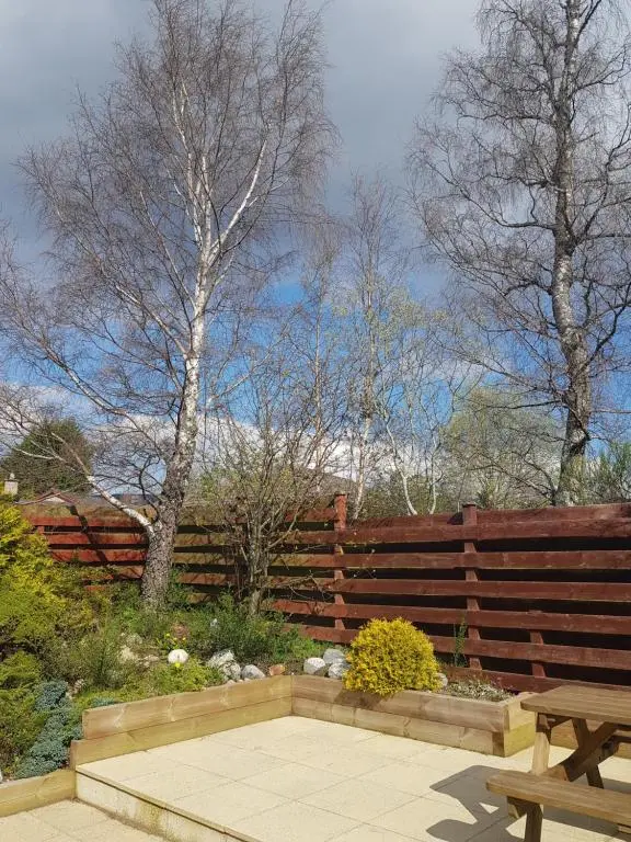 a wooden fence and a bench in a garden at Orange Squirrel Lodge in Aviemore