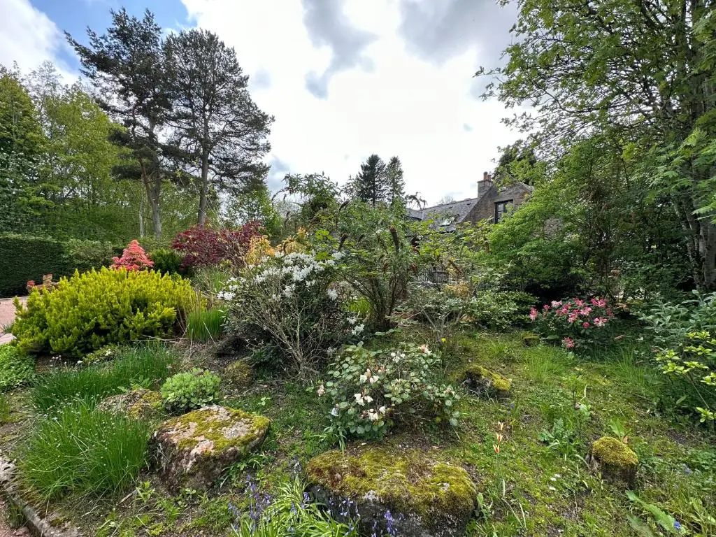 a garden with flowers and rocks and a house at Awakening Alchemy Retreat Centre in Inverurie