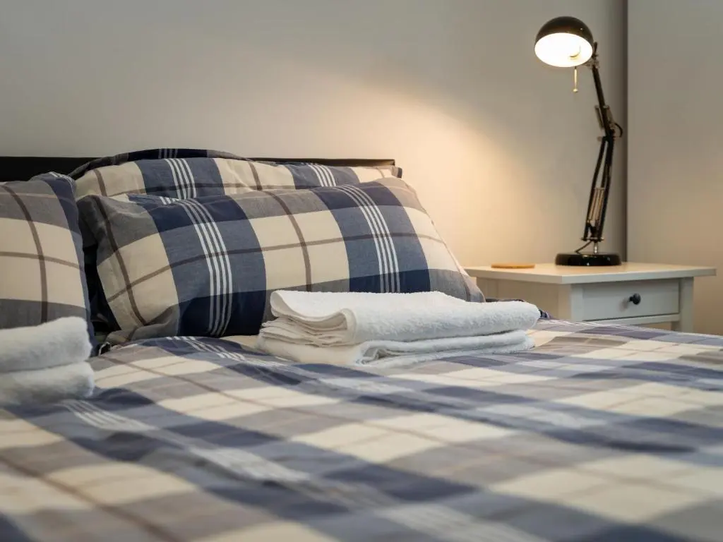 a bed with blue and white plaid sheets and a lamp at Holiday Home Muir Edge by Interhome in Nethy Bridge
