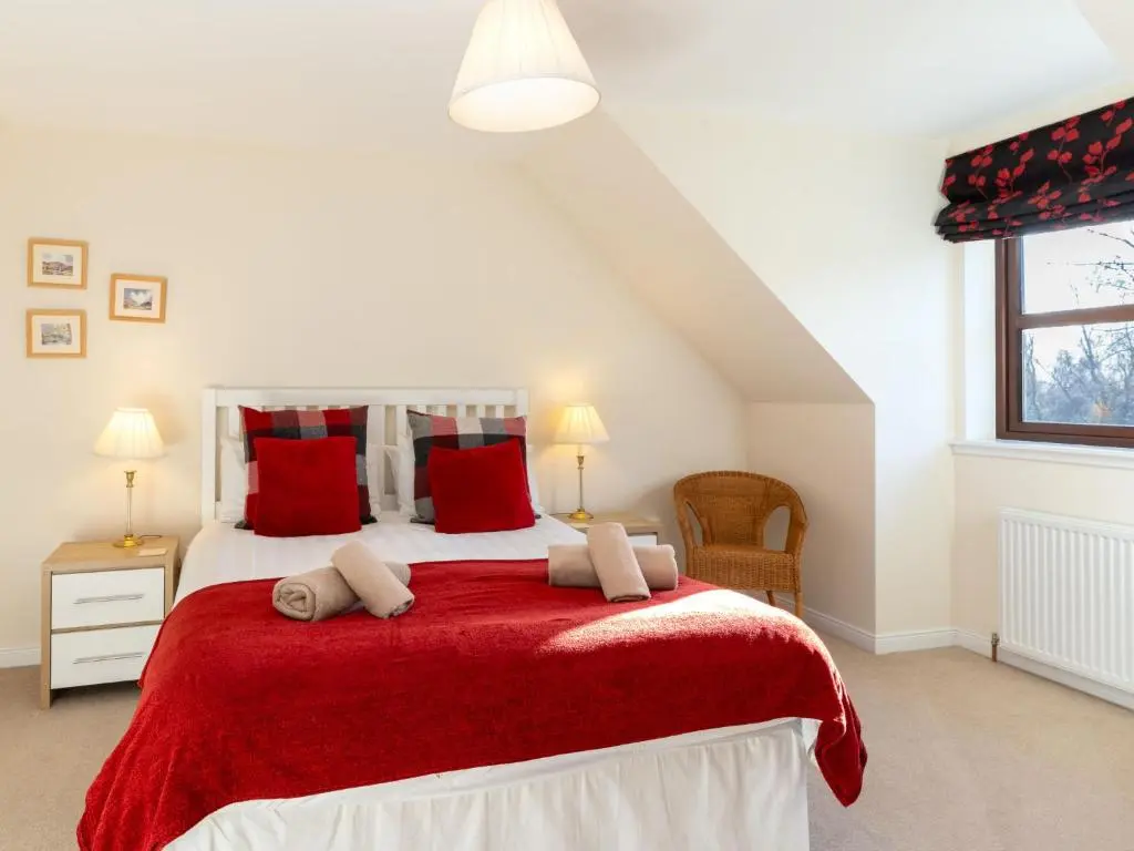 a bedroom with a large bed with red pillows at Villa Pineways by Interhome in Aviemore