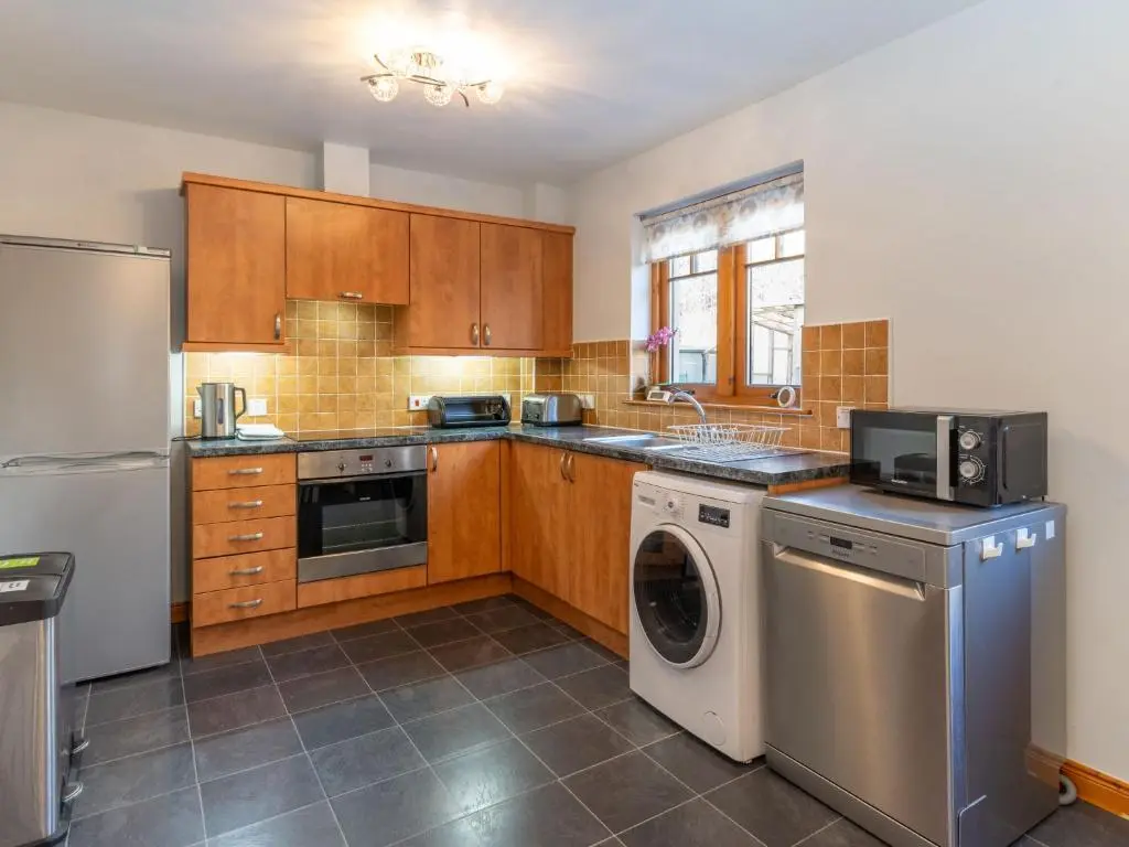 a kitchen with wooden cabinets and a washer and dryer at Holiday Home Cosagach Cottage by Interhome in Aviemore