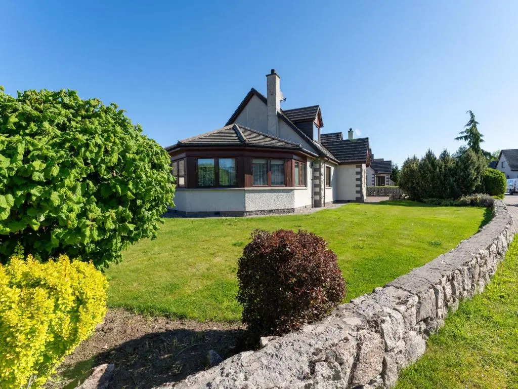 a house with a stone wall in front of a yard at Villa Craigmore Lodge by Interhome in Aviemore