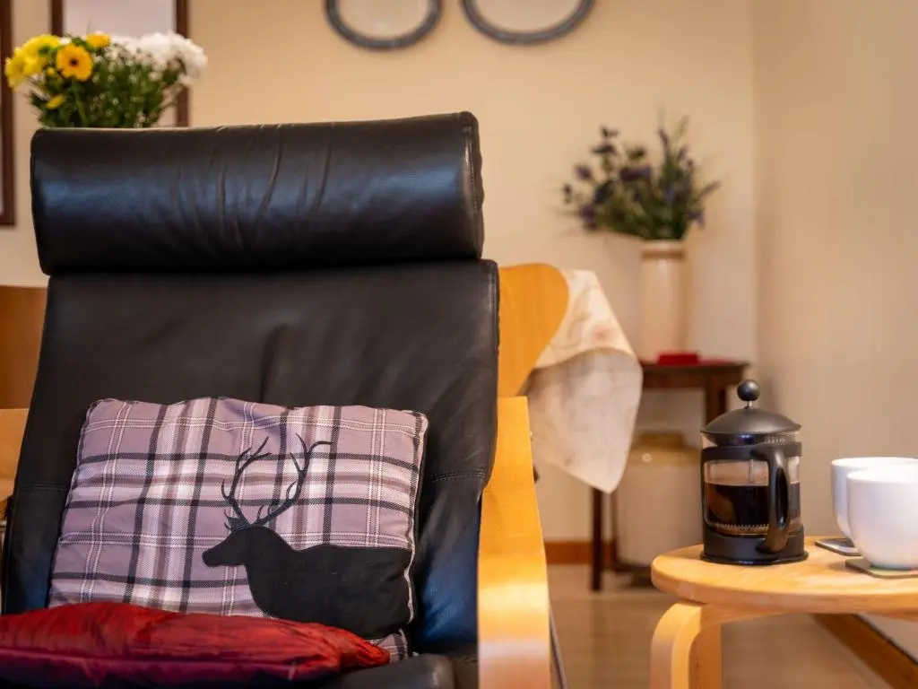 a black leather chair with a pillow with a deer on it at Holiday Home Culduthel by Interhome in Aviemore