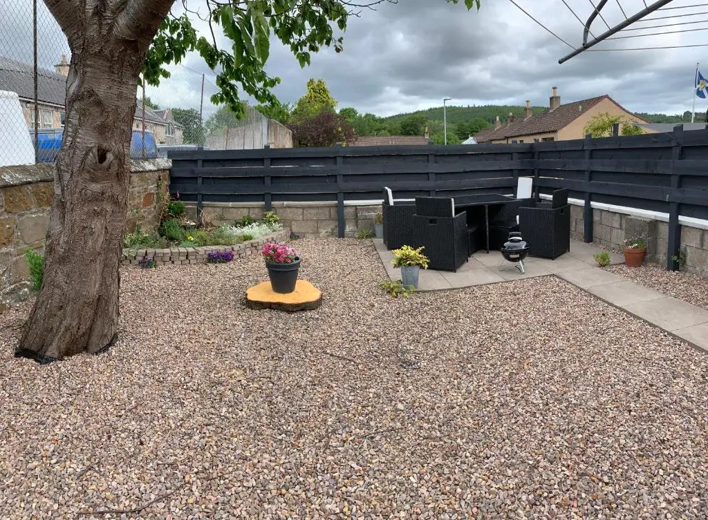a gravel yard with a tree and a table with flowers at No.46, comfortable 2 bedroom property in Rothes