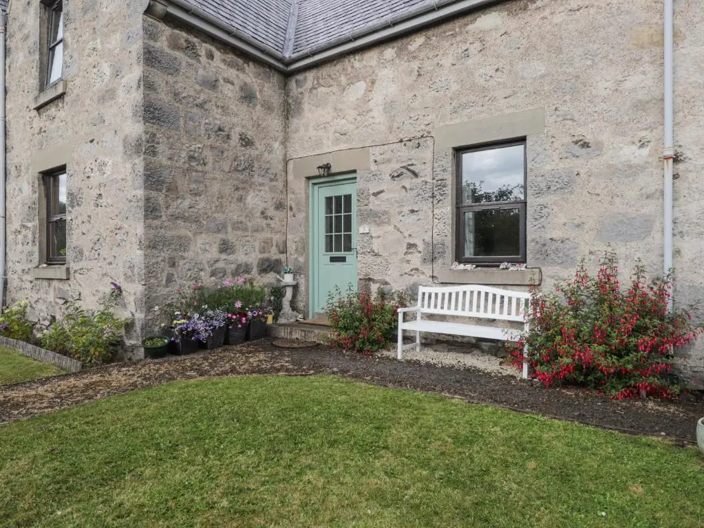 a stone house with a bench in the yard at Rowan Tree House in Brora