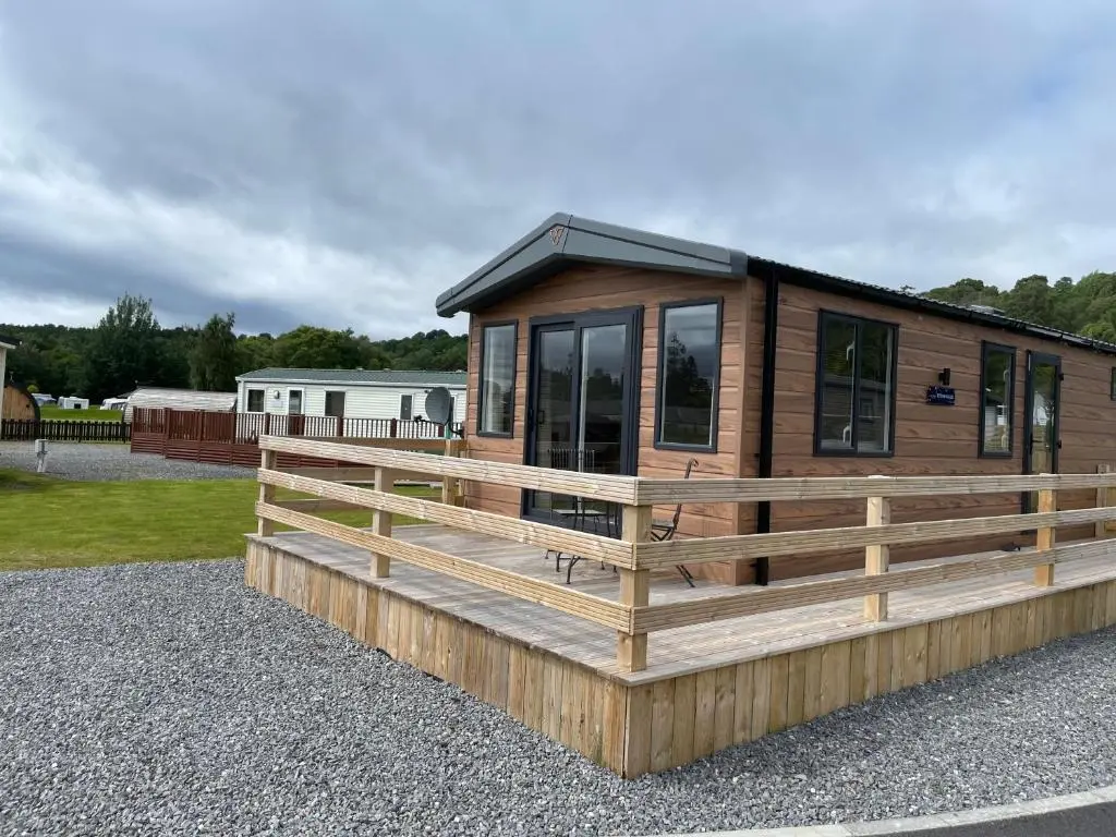 a large wooden cabin with a wooden deck at The Drey in Grantown on Spey