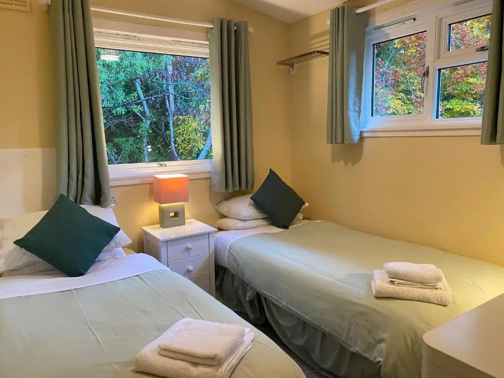 two beds in a room with two windows at Burnside Chalet on Reelig Estate in Kirkhill