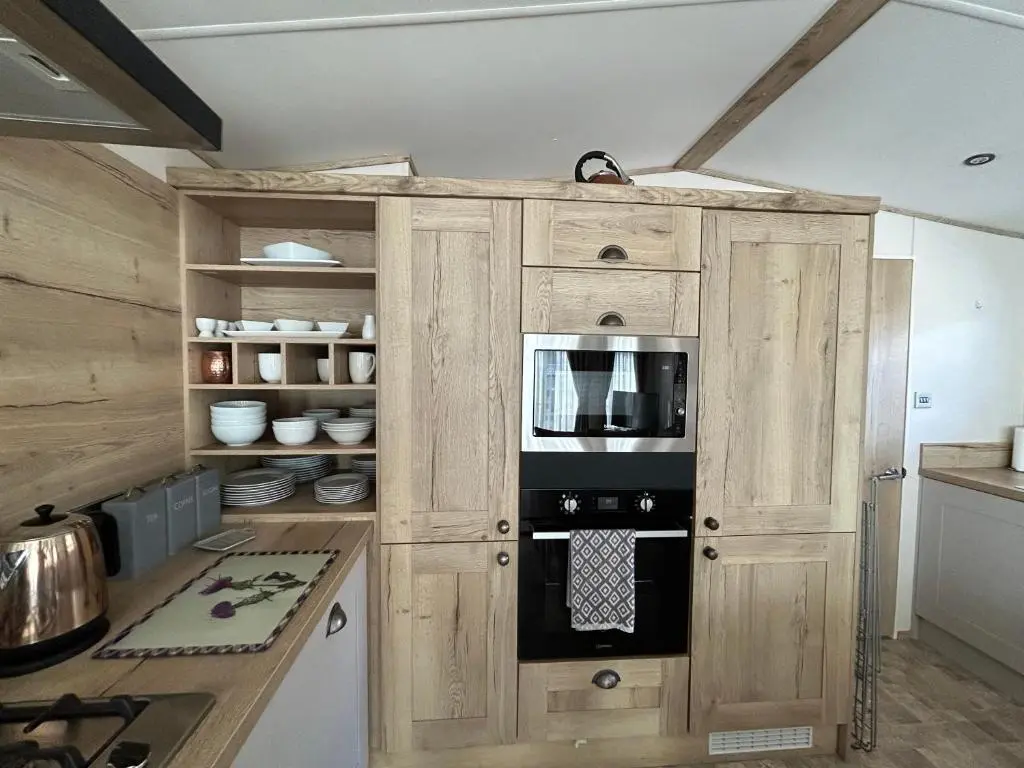 a kitchen with a wooden cabinet with a microwave at Lodge 2 The Wee Hut Aviemore in Aviemore