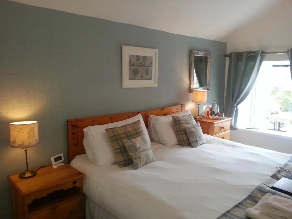 a bedroom with a bed with white sheets and pillows at Ardlogie Guest House in Aviemore