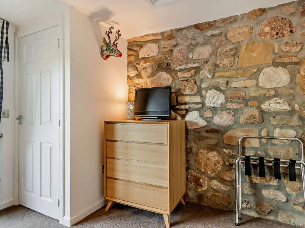 a tv on a wooden dresser next to a stone wall at 1 Bed in Elgin 32129 in Burghead