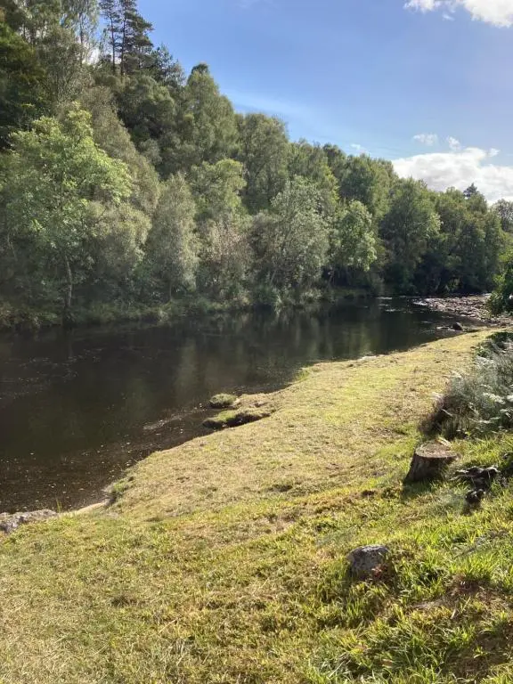 a river with grass and trees on the side at Invercassley cottage in Lairg