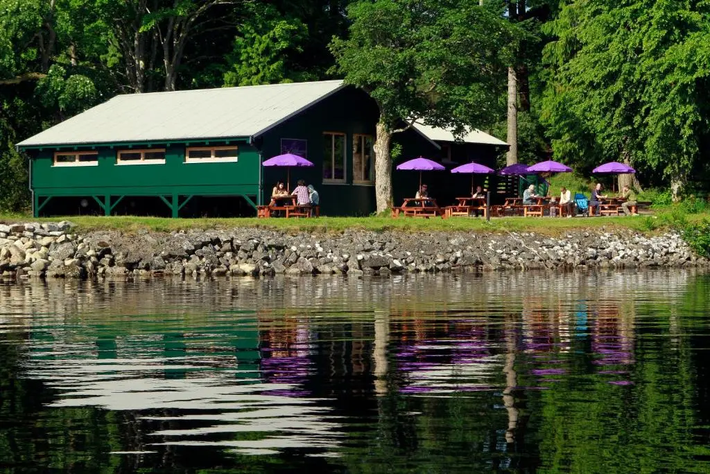 a building with tables and purple umbrellas near a body of water at Noble Apartment - Highland Club in Fort Augustus