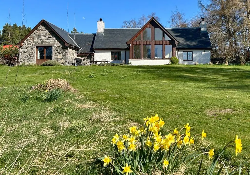 a house with yellow flowers in front of a yard at Drumguish Cottage in Kingussie